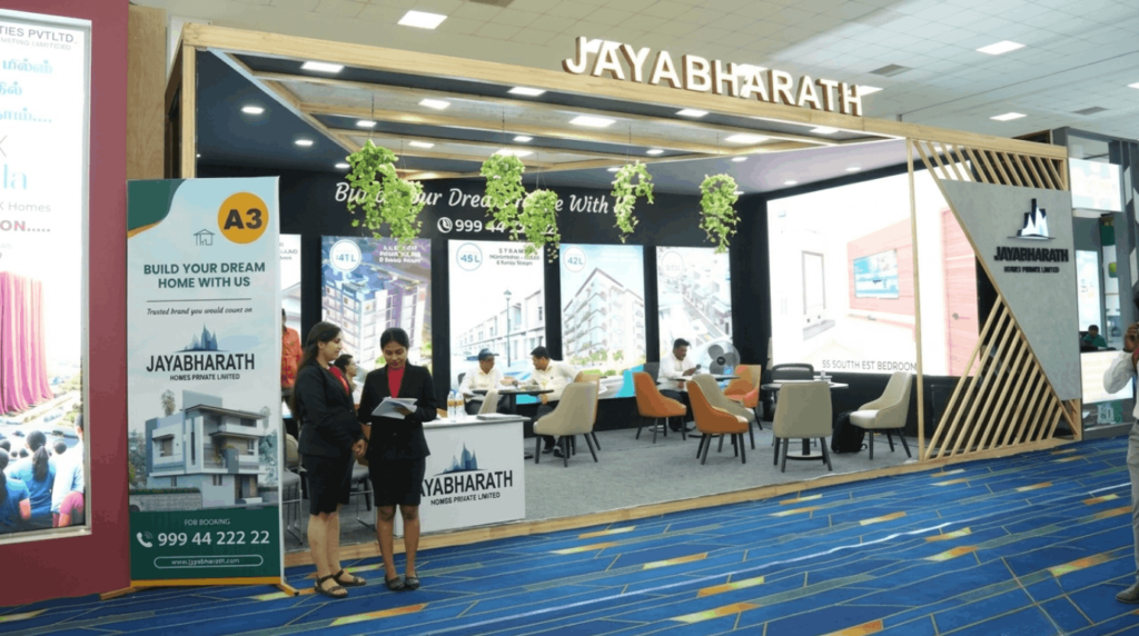 Visitors comparing apartment, villa, and residential plot options at a real estate exhibition, reviewing brochures, floor plans, layout maps, and property information.