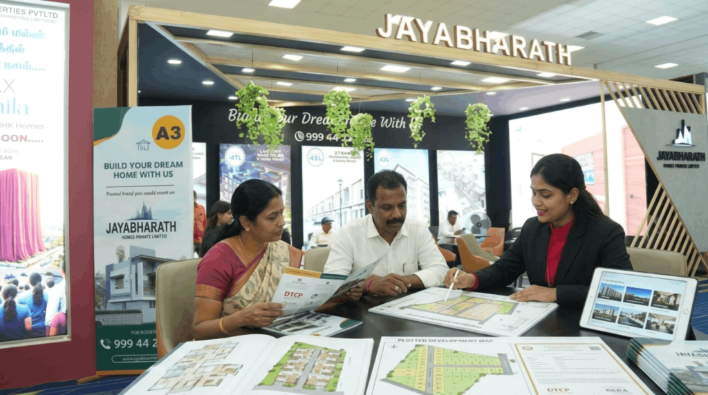 Prospective homebuyers consulting with a real estate advisor at an exhibition stall while reviewing apartment floor plans, villa layouts, plotted maps, and approval documents.
